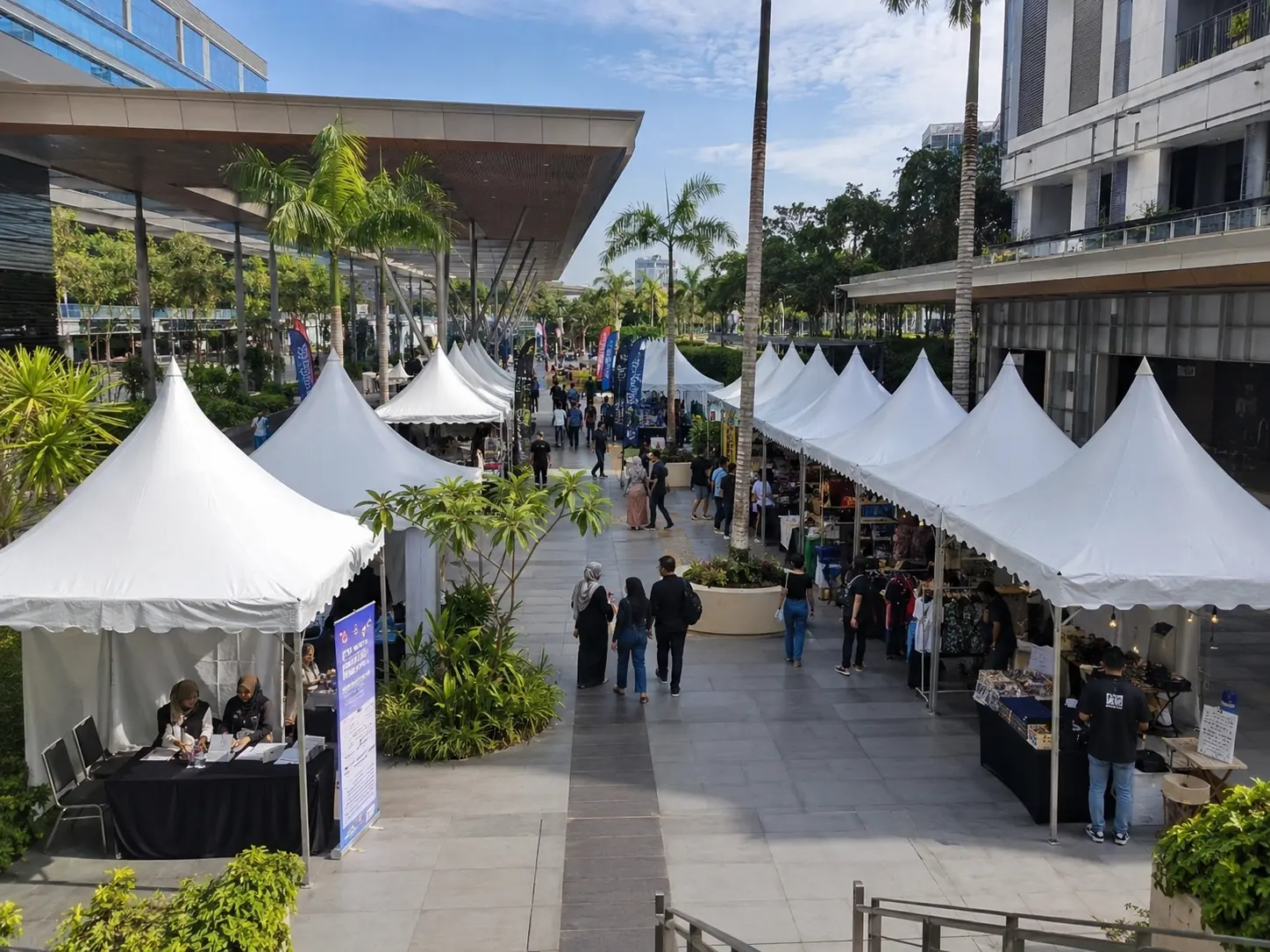 White bazaar canopy tents arranged in an urban courtyard market setup in Malaysia with palm trees, vendor booths and visitors walking through the bazaar