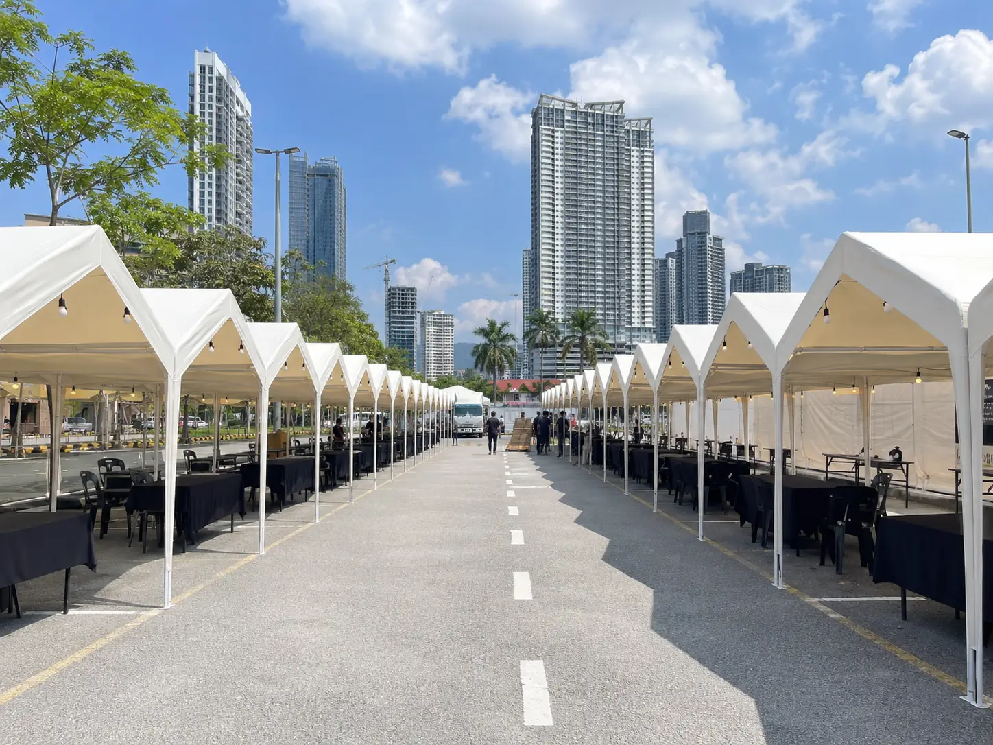 City market setup in Malaysia with long rows of white bazaar tents, black table covers and high-rise buildings in the background
