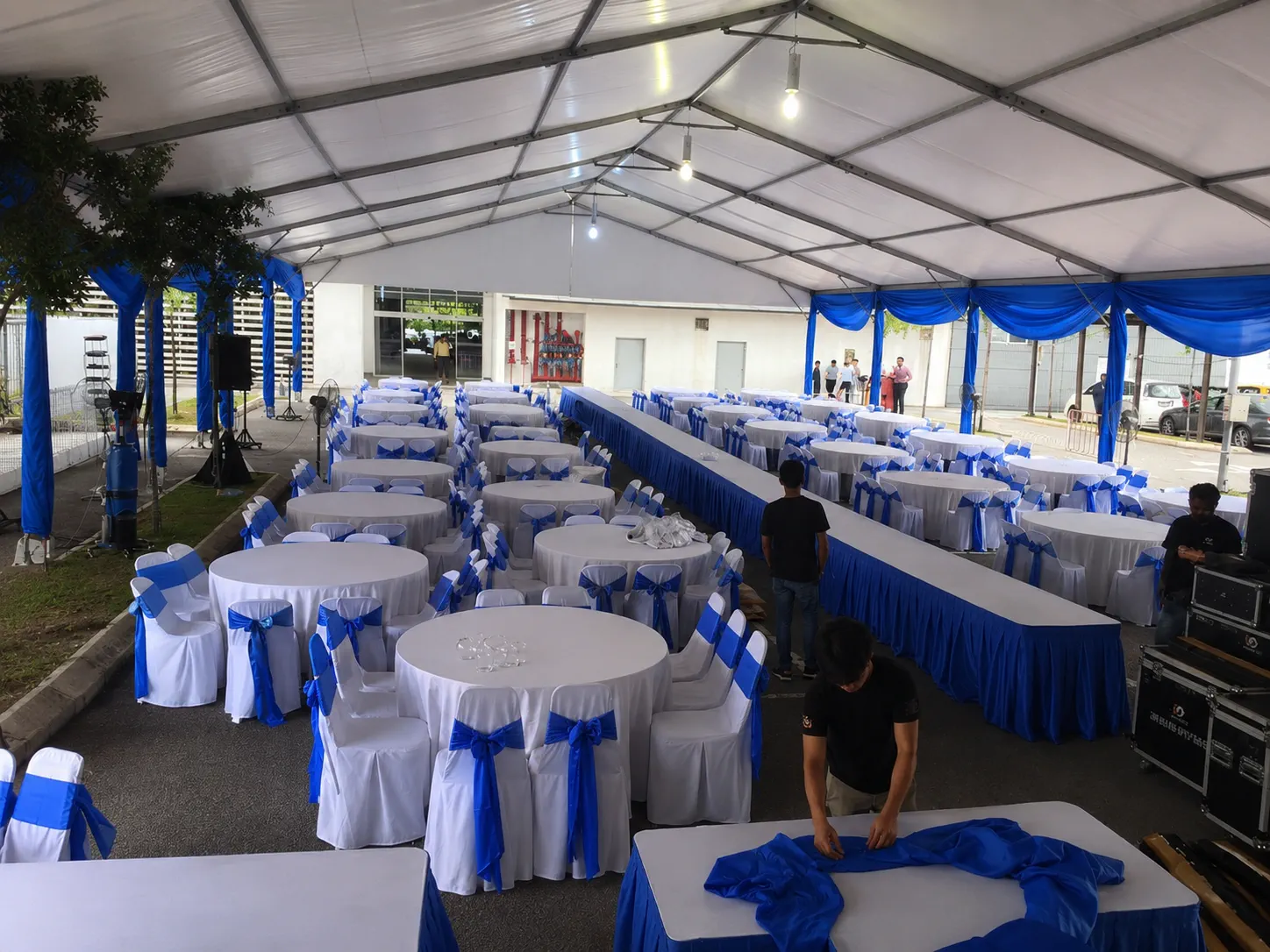 Blue and white banquet marquee layout with round dining tables, blue chair ribbons, long head table, sound equipment and covered guest area