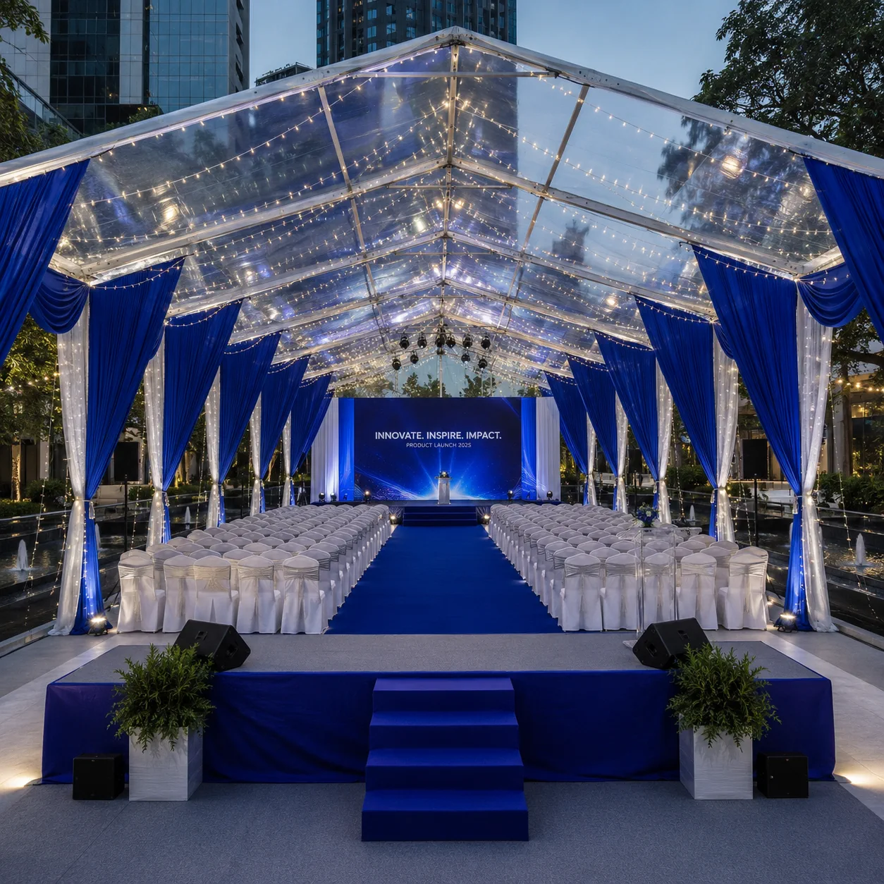 Clear roof product launch marquee with blue and white drapes, theatre seating, blue carpet aisle, stage platform, LED backdrop, speakers and warm fairy lights
