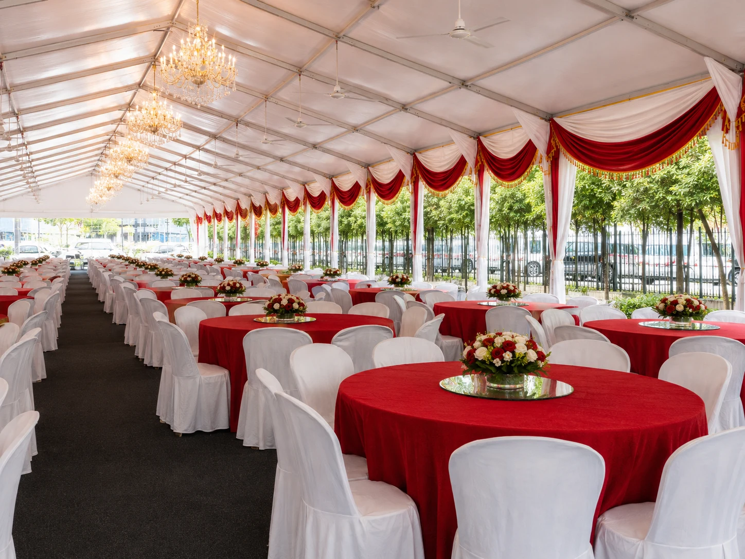 Angled view of chandelier wedding marquee dining layout with red tablecloths, white chair covers, floral centrepieces and red-white side drapes