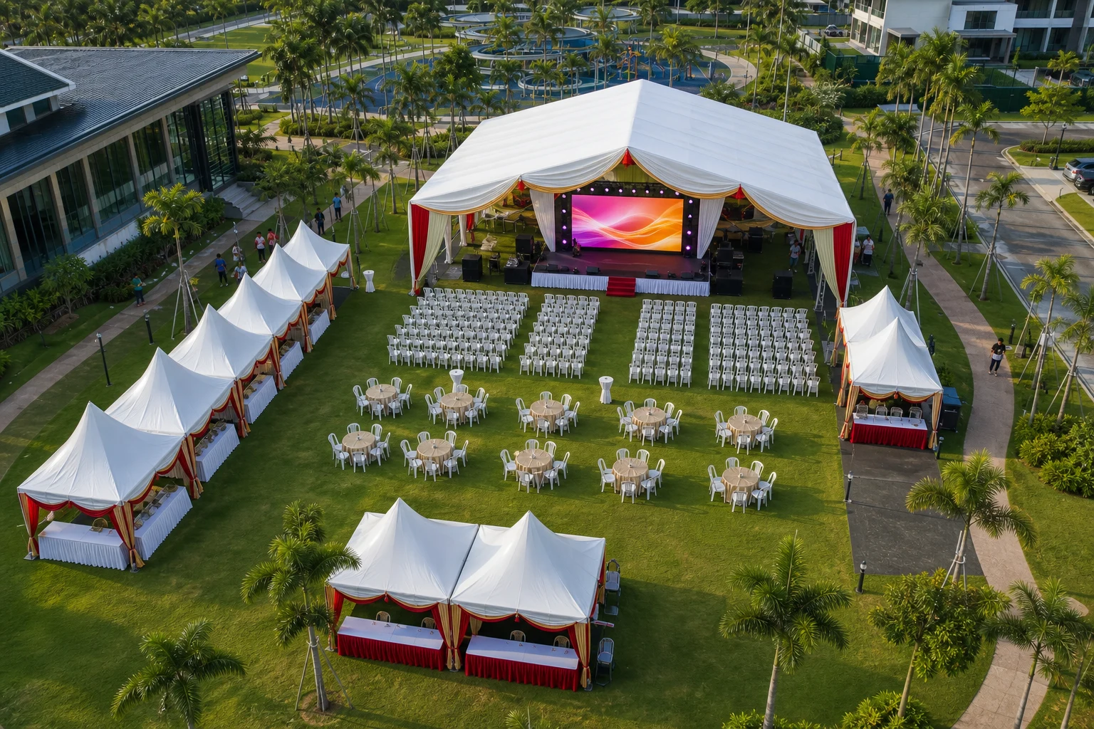 High angle view of Gamuda Gardens Rawang event lawn layout with open marquee, centered lit LED screen on stage, chair rows, dining tables and food canopies