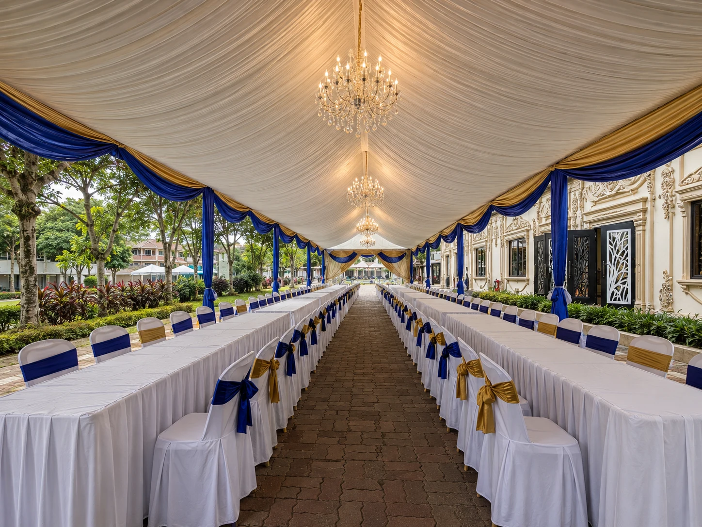 Long table marquee layout with blue and gold chair ribbons, chandelier lighting, white table skirting and covered central walkway