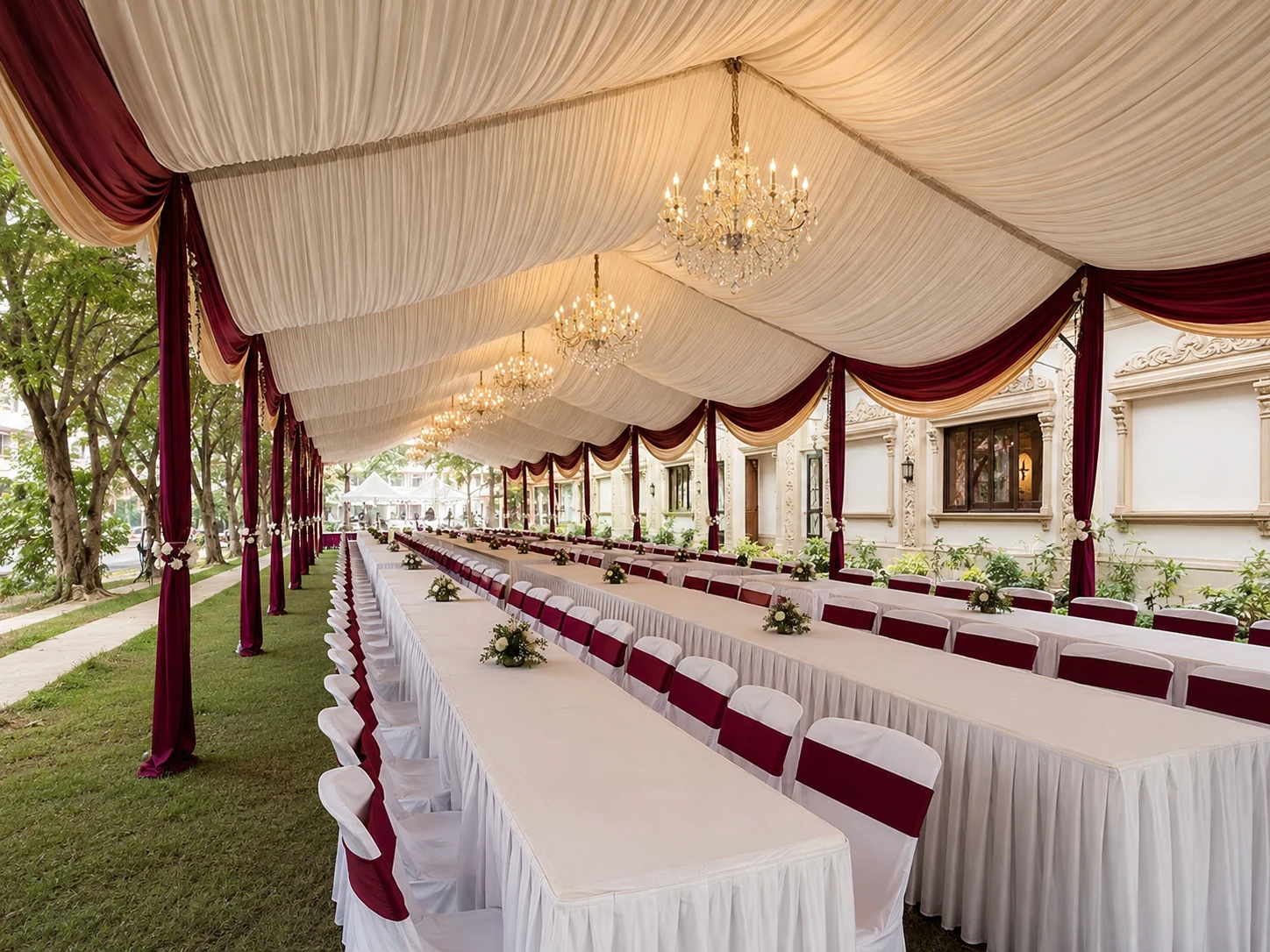 Burgundy long table marquee layout with cream ceiling drapes, chandelier lighting, white table skirting and garden-side seating