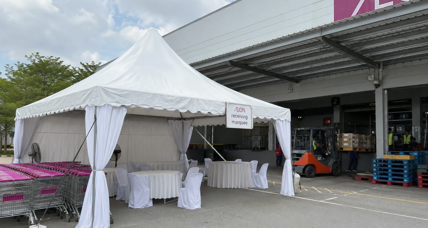 White canopy marquee at a retail receiving bay with forklift activity, tables and loading access