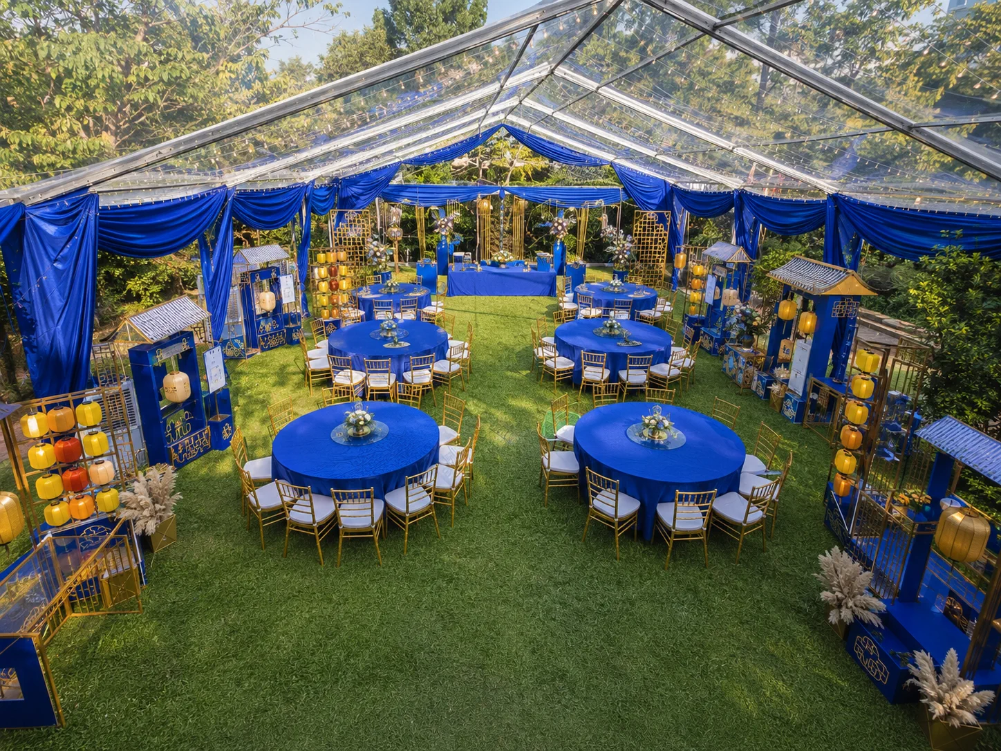 High angle view of royal blue clear roof banquet marquee layout with round blue tables, gold chairs, lantern booths, stage area and transparent roof panels