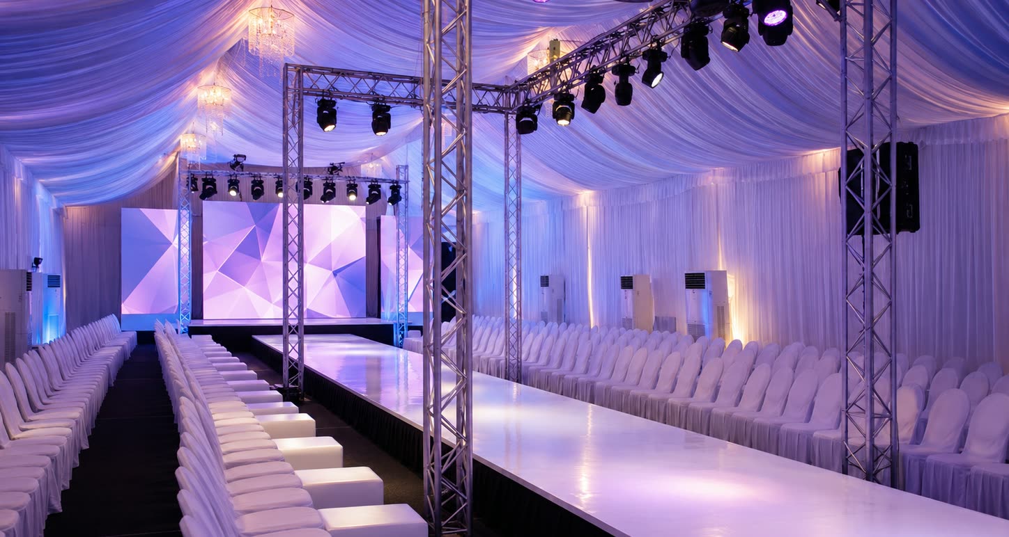 Production marquee with runway stage, white chair seating, truss lighting and pearl draped ceiling