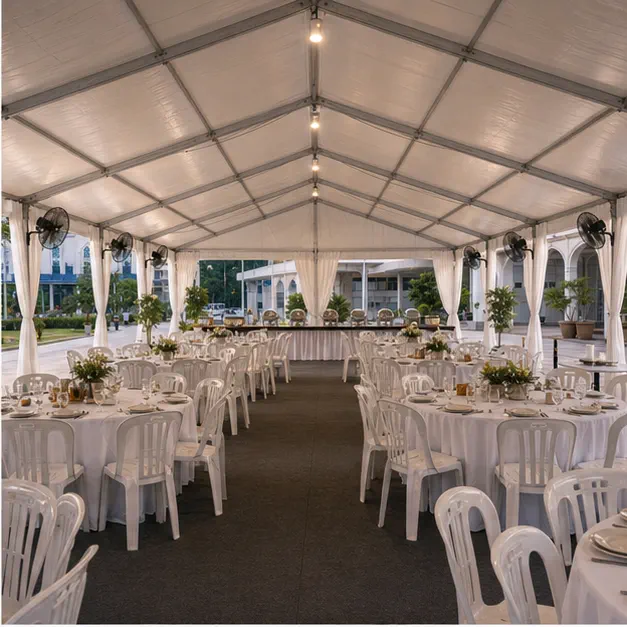 Inside view of a white marquee with dining tables, plastic chairs, fans, side drapes and warm community meal lighting