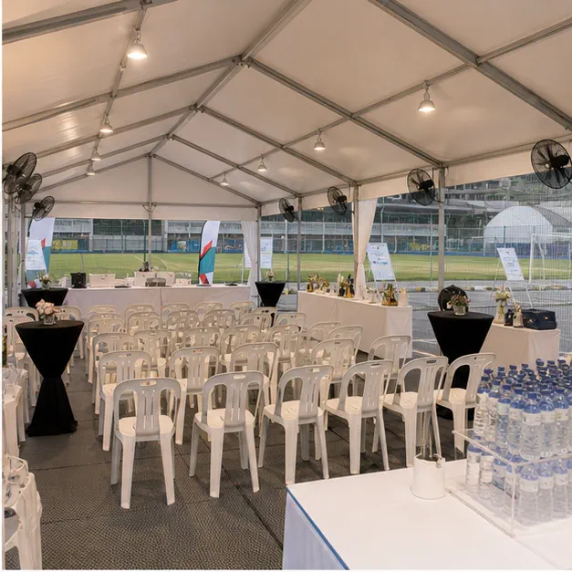 Inside view of a stadium event marquee with spectator shade seating, plastic chairs, fans, hydration table and prize table