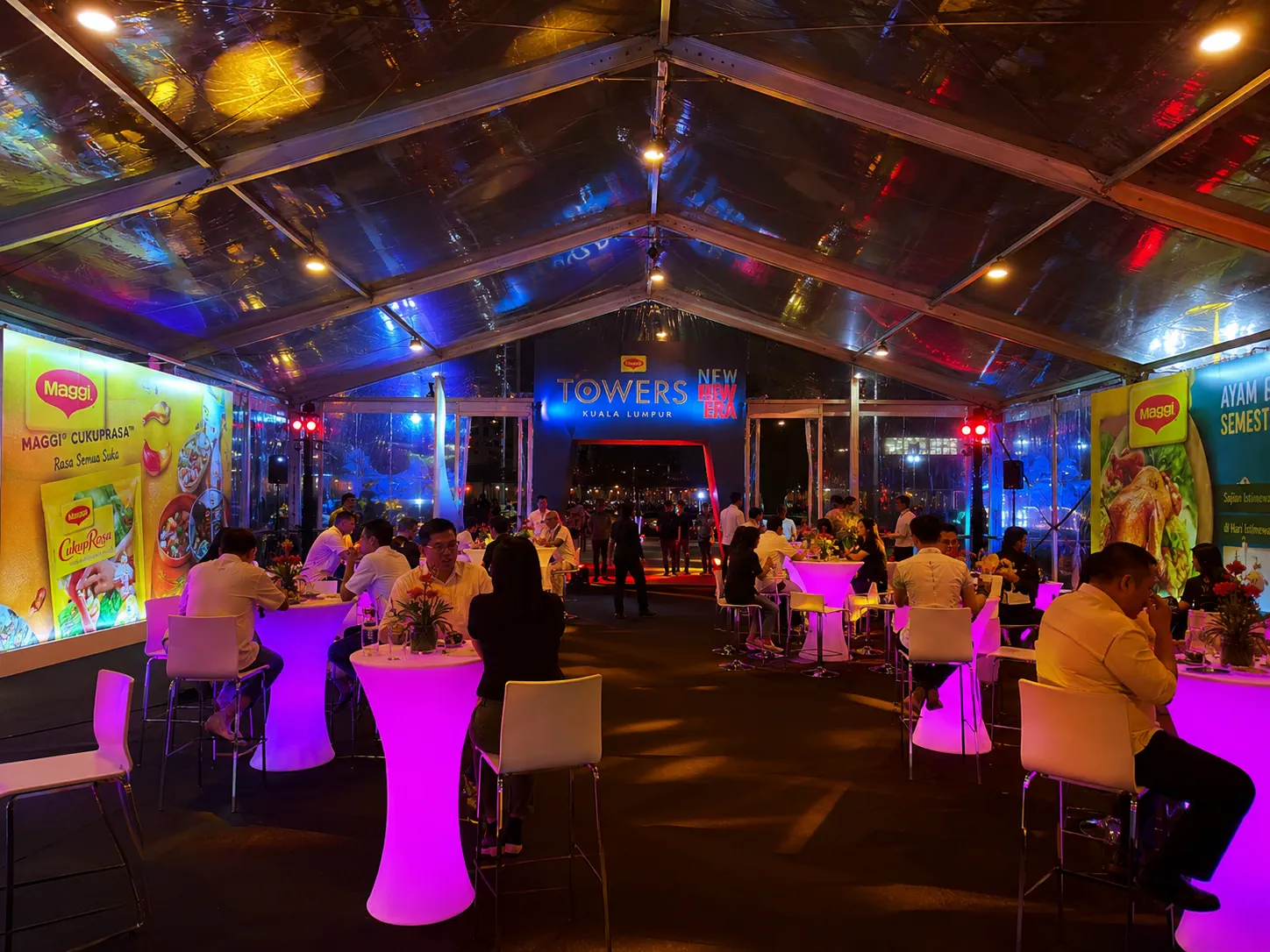 Interior clear roof product activation marquee with cocktail tables, guest seating, brand display walls, coloured lighting and open central walkway