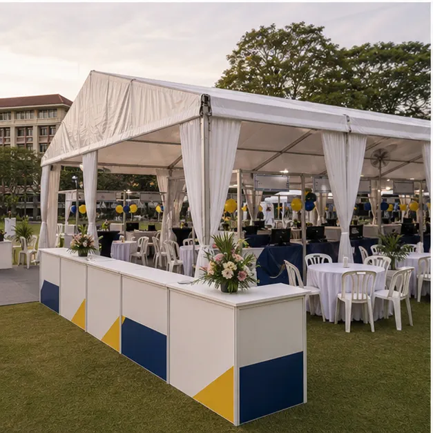 Side view of university campus marquee setup with registration desk, student carnival counters, chairs and shaded walkway
