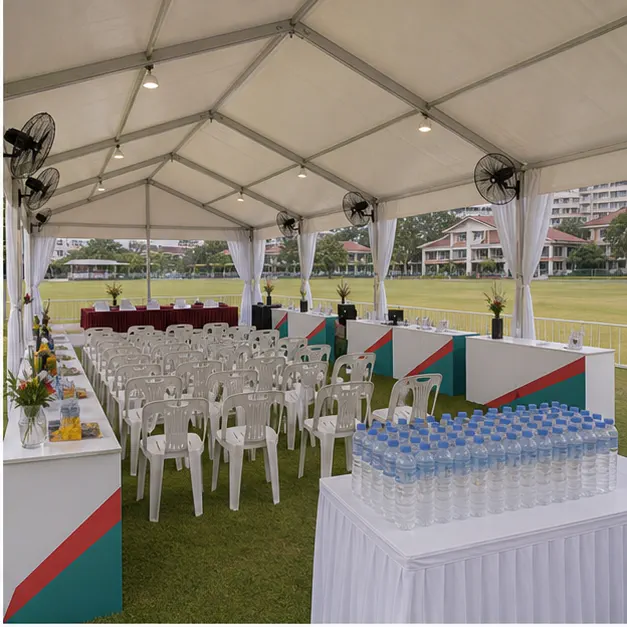 Inside view of open field marquee with shaded seating, support counters, fans, water station and campus event setup