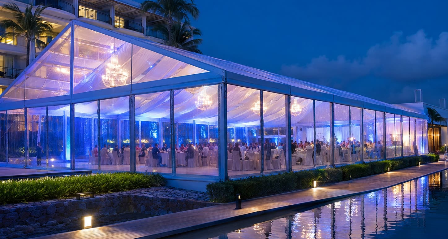 Blue lit transparent marquee beside water at night with chandeliers and reflected lights