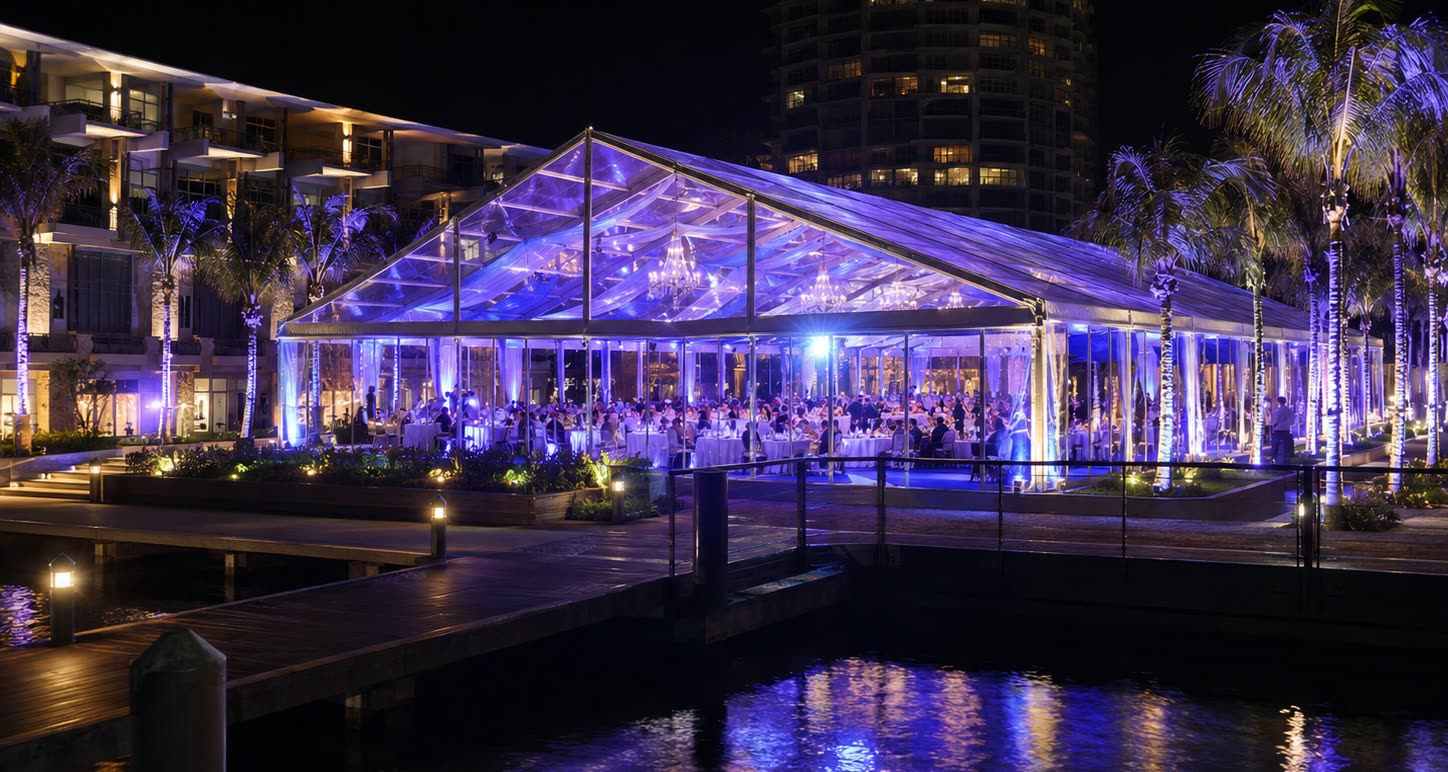 Waterfront transparent marquee tent with blue lighting and palm trees at night