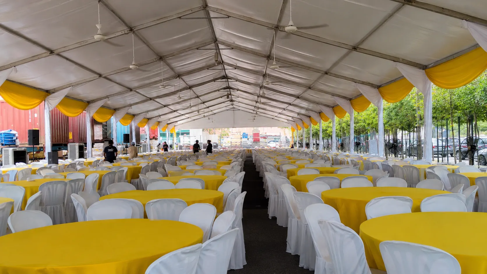 Large white marquee dining setup with yellow drapes, yellow round tables, white chair covers, ceiling fans, side fans and central service aisle