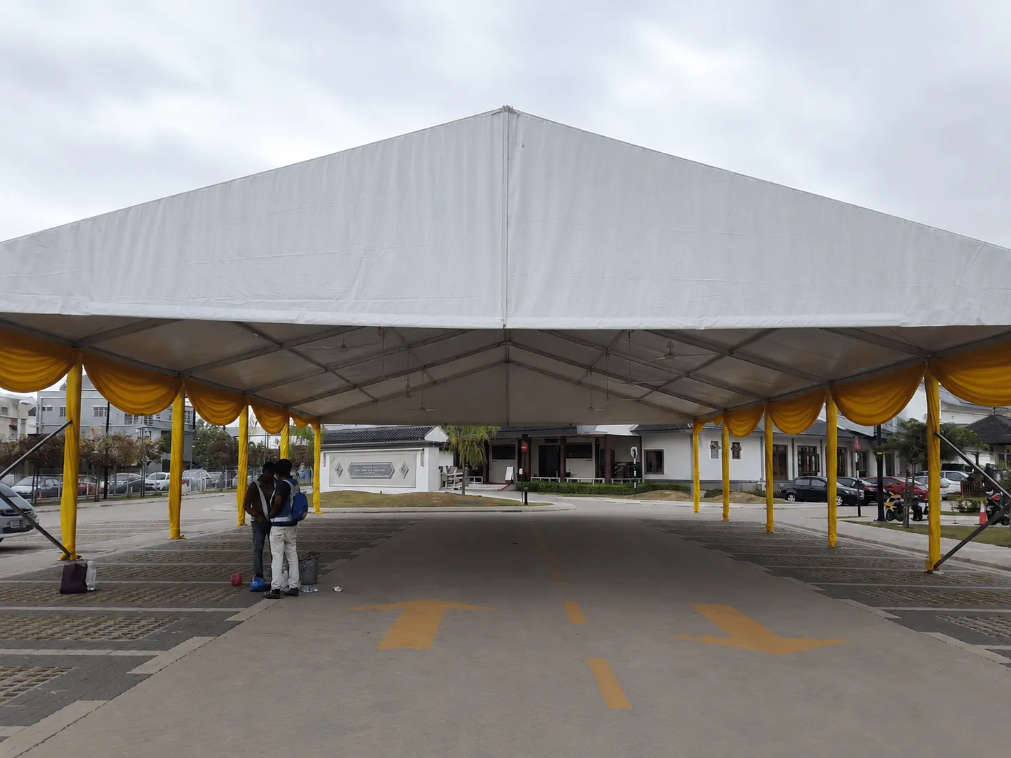 Exterior view of a large white marquee with yellow drapes, open road-facing entrance, covered dining area and compound access route